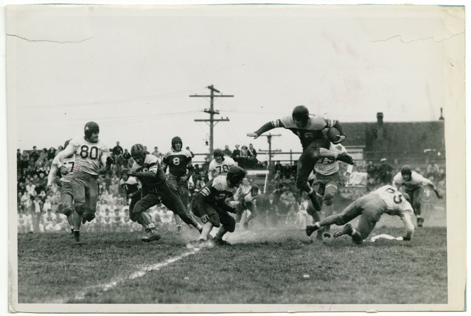 Chimacum fullback Jim Parker (16) leaps over Townsend defensive player Don Lindley (65), as Townsend team captain Don Brecht (80) draws a bead on Parker. Game played at Flint Field Sept. 20, 1946.